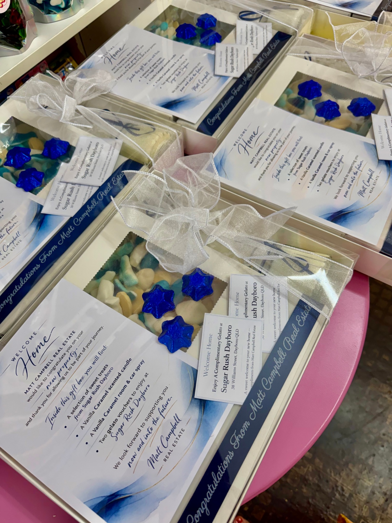 Set of Matt Campbell Real Estate Congratulations gift boxes with white organza bows and blue star chocolates