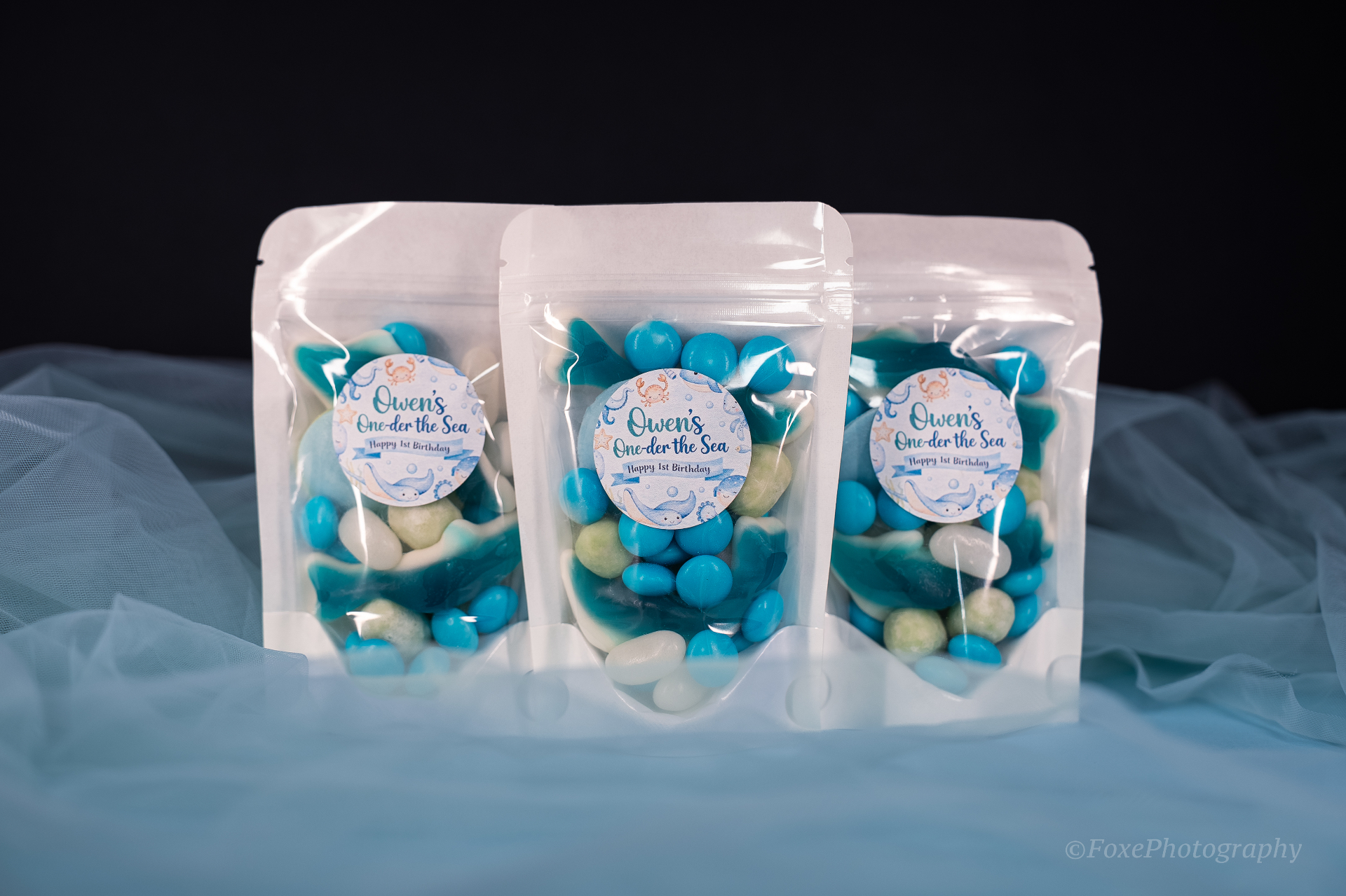 Under-the-sea themed party favour bags with blue and white lollies and personalised 'Owen's One-der the Sea' first birthday labels